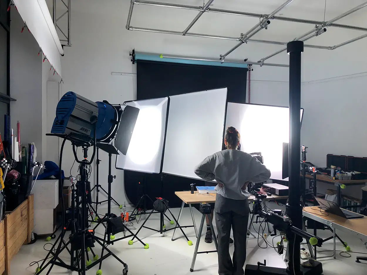 Photographe de dos devant un setup d'éclairage professionnel en studio — softboxes larges, projecteur ARRI et fond motorisé noir déployé, plateau Greystone Studio à Villeurbanne