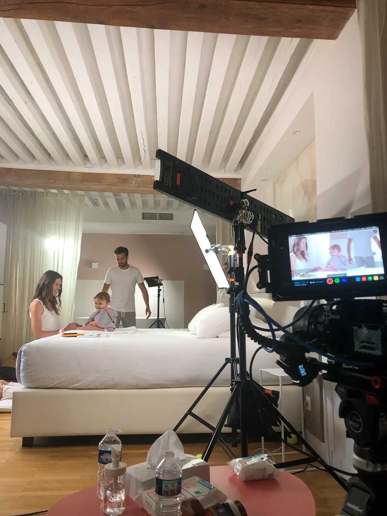 Tournage publicitaire famille avec caméra cinéma sur Sachtler, panneau LED et moniteur externe, décor chambre avec lit blanc, production vidéo professionnelle
