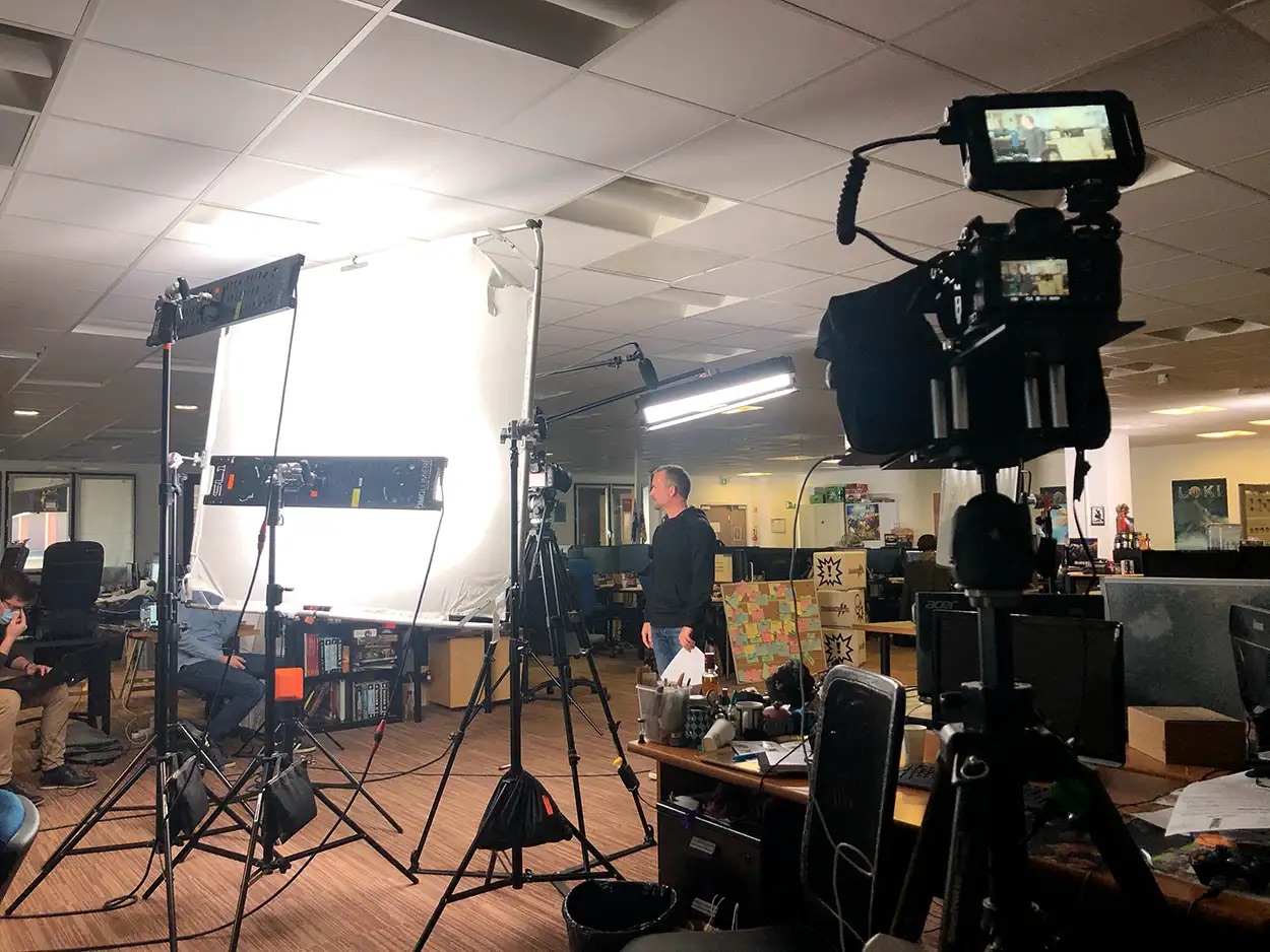 Tournage vidéo corporate en open space avec panneau LED, diffuseur blanc et caméra cinéma sur trépied, équipe de production sur plateau hors studio