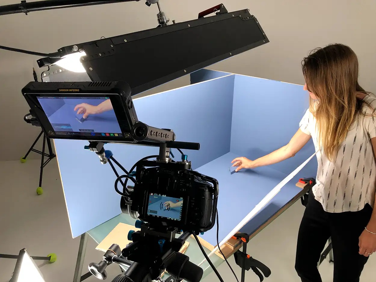 Opératrice réglant un produit dans un cube blanc sur fond bleu, moniteur Shogun Inferno en amorce, tournage Greystone Studio Lyon