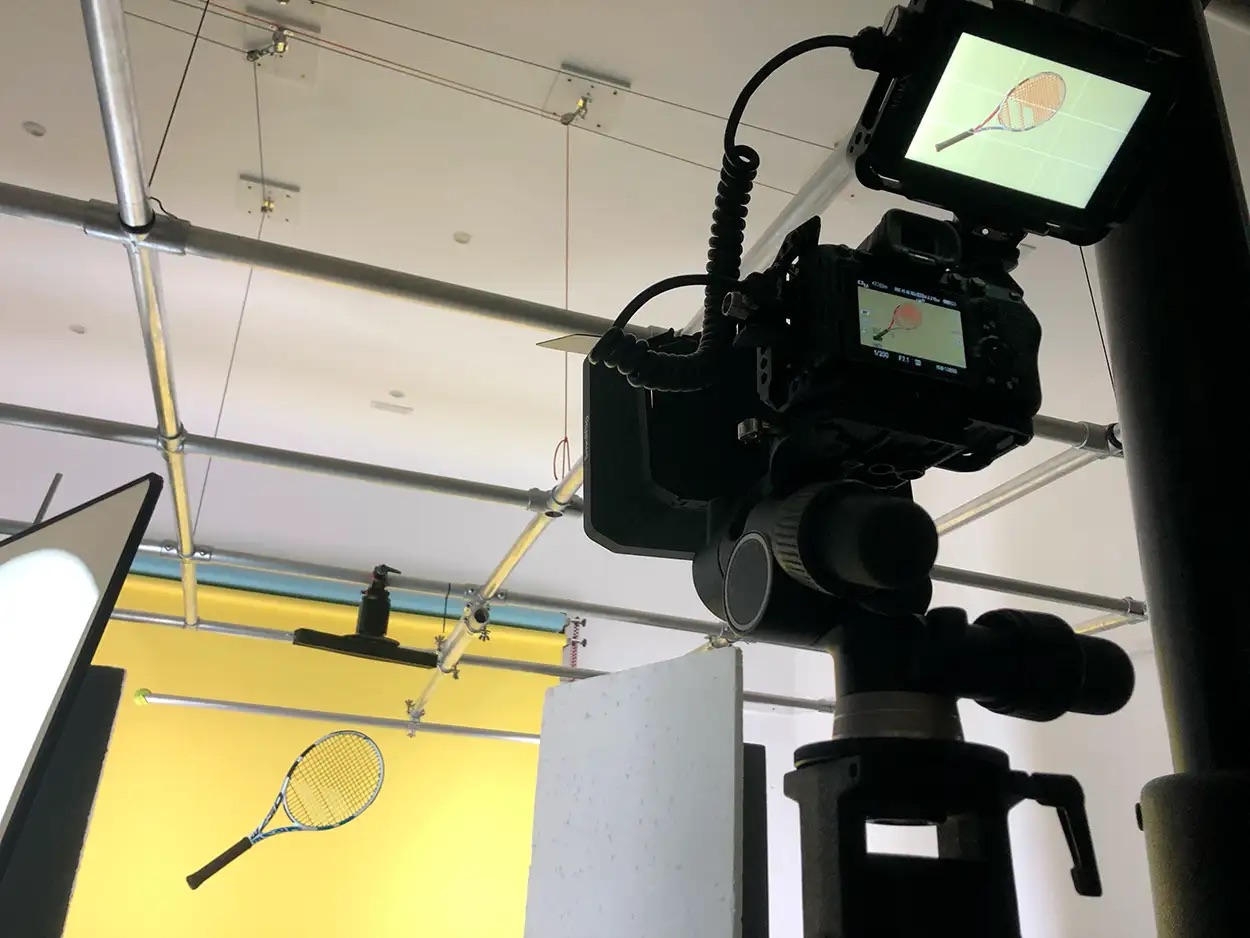Caméra en cage avec moniteur externe filmant une raquette de tennis suspendue sur fond jaune motorisé, Greystone Studio Lyon