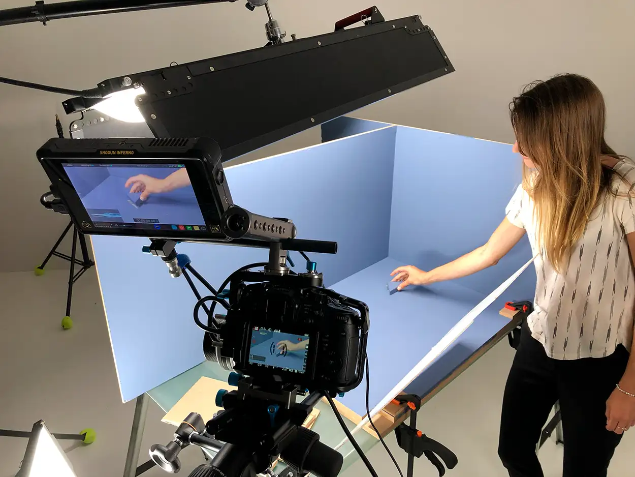 Opératrice réglant un produit dans un cube blanc sur fond bleu, moniteur Shogun Inferno en amorce, tournage Greystone Studio Lyon