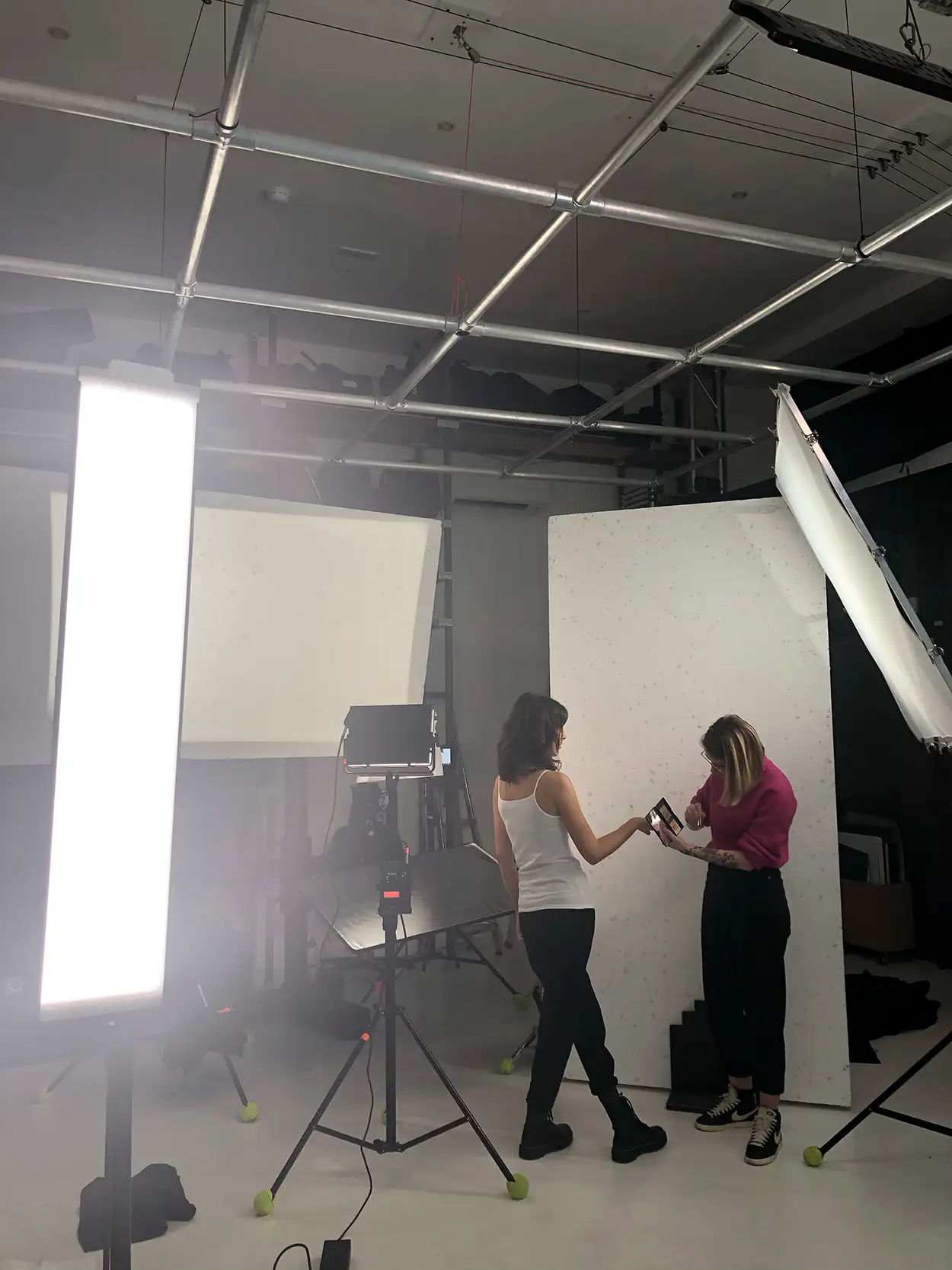 Deux personnes consultant un moniteur sur plateau de tournage blanc avec panneau LED tubulaire, Greystone Studio Villeurbanne