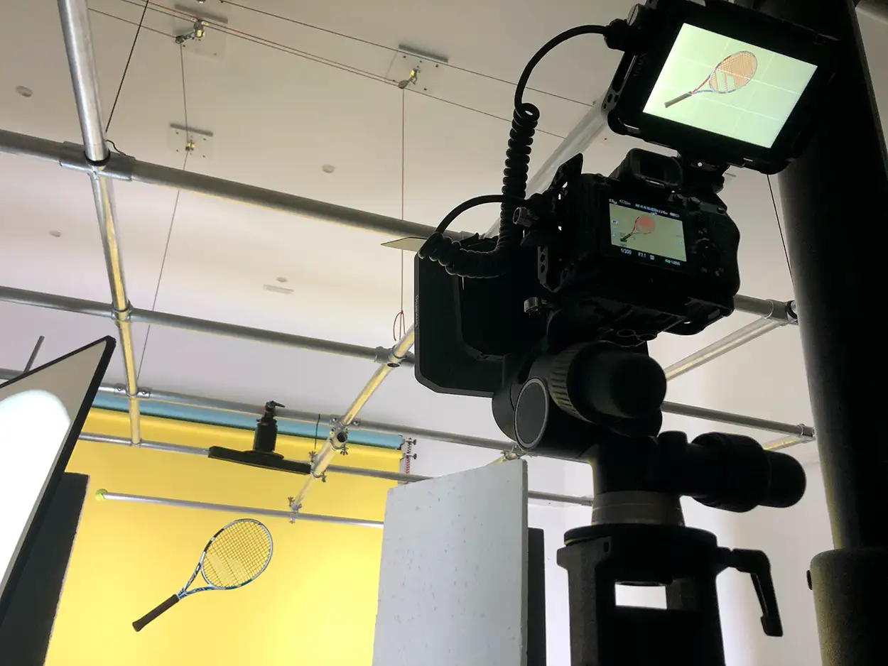 Caméra en cage avec moniteur externe filmant une raquette de tennis suspendue sur fond jaune motorisé, Greystone Studio Lyon